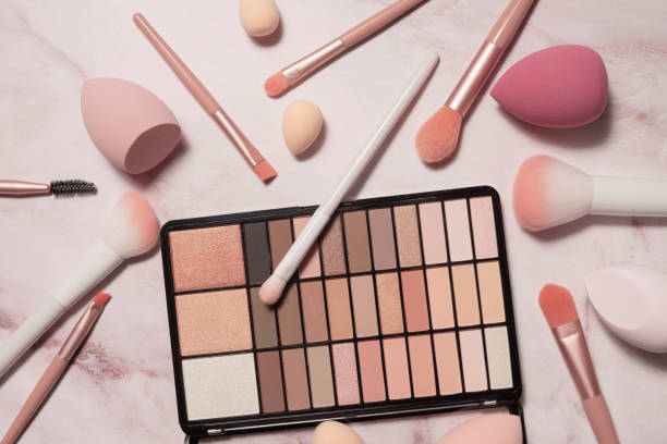 An array of makeup essentials including brushes, sponges, and an eyeshadow palette on a marble surface.