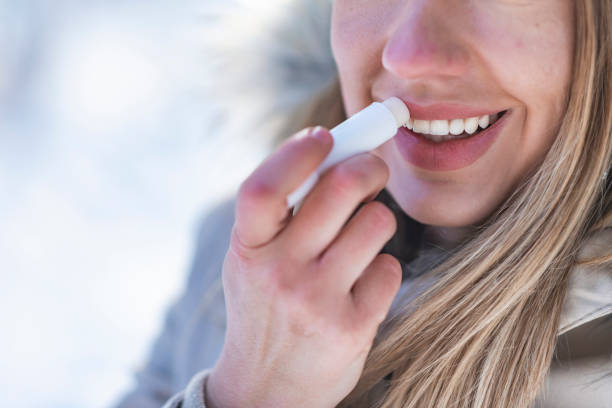 Woman applying lip balm to her dry lips as a preparation step before applying lipstick.